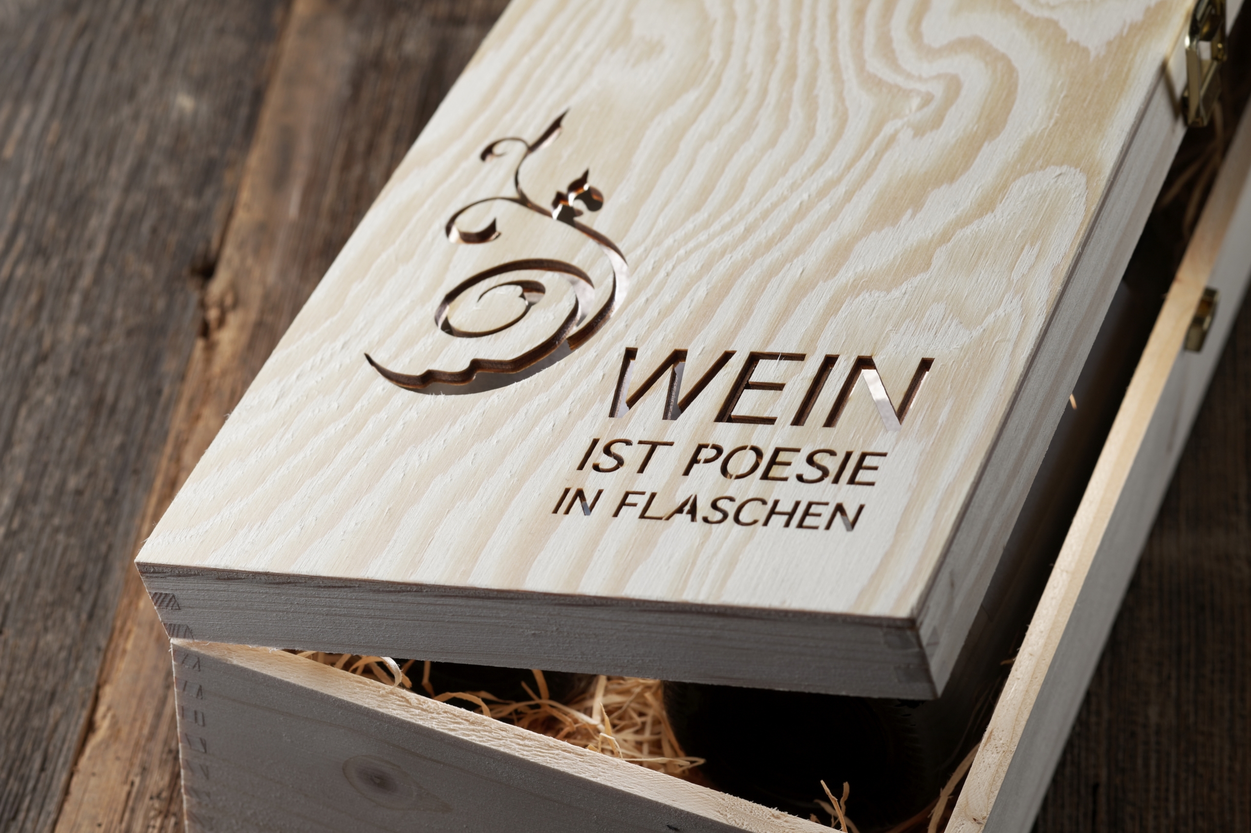 Teilweise geöffnete Holzkiste mit geschwungener Verzierung und der Aufschrift „Wein ist Poesie in Flaschen“.