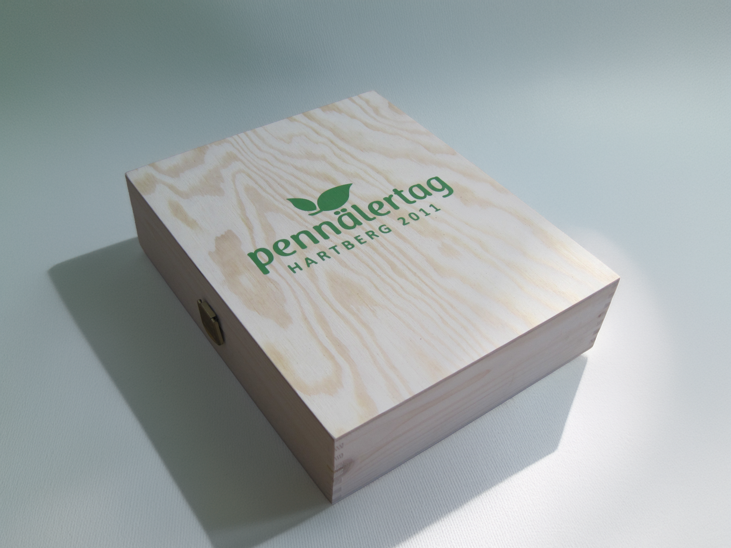 Flache Holzkassette mit grünem Blattmotiv und der Aufschrift „pennälertag – Hartberg 2011“.