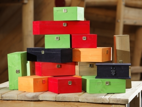 Gestapelte Holzkassetten in Grün, Rot, Orange, Dunkelblau und Naturfarbe mit Metallverschlüssen.